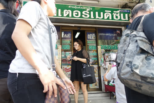 A customer examining her recently purchased medical products outside a pharmacy near Bangkok's Victory Monument. The name of the shop is "Doctor Medicine". 