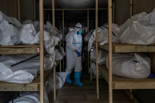 Workers at a Brooklyn hospital retrieving a body from a refrigerated trailer in April.Credit...Victor J. Blue for The New York Times